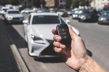 Close-up of a woman unlocking a car using a key fob, with a white car parked in a car park in the background.