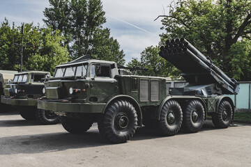 Military vehicle Rocket artillery with camouflage coloring stands in a car park. Background of nature and trees.