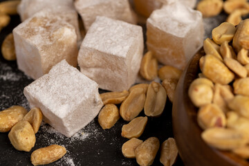 square Turkish delight in powdered sugar with nuts inside, scattered oriental sweets Turkish delight with peanuts on a black slate board, closeup