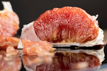 red citrus on the black mirror, peeled citrus grapefruit with red flesh, the fruit is reflected on a black mirror surface