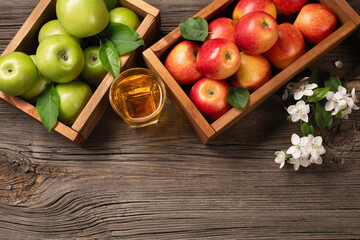 Ripe red and green apples in wooden box with branch of white flowers and glass of fresh juice on a wooden table