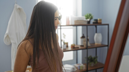 Woman smiling indoors in a serene spa room reflecting on wellness, surrounded by elegant decor and natural light, embodying beauty and relaxation in a calming setting.