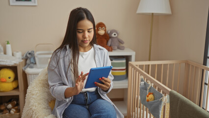 Woman using tablet in cozy bedroom with baby cradle and toys, showcasing a relaxed indoor home...