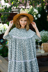Beautiful girl in dress and hat standing near table in summer in garden