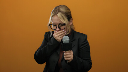 Woman reporter holding microphone over isolated orange background expressing emotions in black...