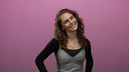 Woman smiling against pink background with curly hair exuding joy and confidence.