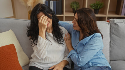 Women comforting each other on a cozy couch in a serene living room showcasing friendship and...