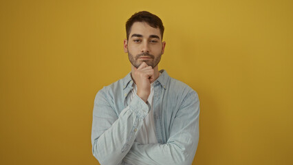 Fototapeta premium Young man with thoughtful expression standing over isolated yellow background suggesting introspection and focus on personal growth and development