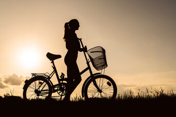 Silhouette of a woman with a bicycle. Sunset background.