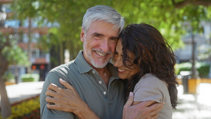 Fototapeta premium Middle-aged couple embraces lovingly in an outdoor urban park setting, capturing the essence of a happy relationship between man and woman in a serene city environment.
