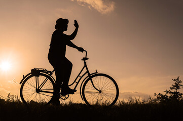 Silhouette of a male cyclist in a hat on a bicycle. Sunset background.