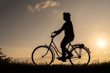 Silhouette of a male cyclist in a hat on a bicycle at sunset.