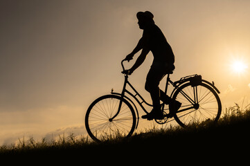 The silhouette of a cyclist in a hat on a bicycle descends the mountainside at sunset.