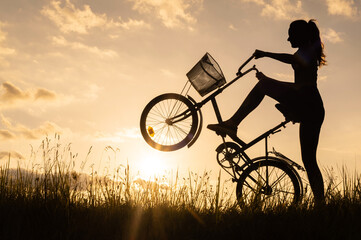 A silhouette of a cyclist woman holding and standing on the back wheel of a bicycle or bike. Sunset...