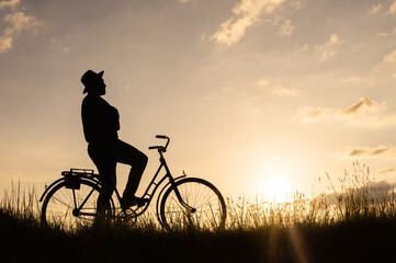 Silhouette of a cyclist sitting on a bicycle and enjoying the sunset on a field in a meadow.