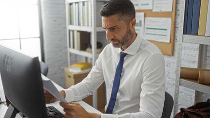 Professional man working in office focusing on documents with shelves in background suggesting...