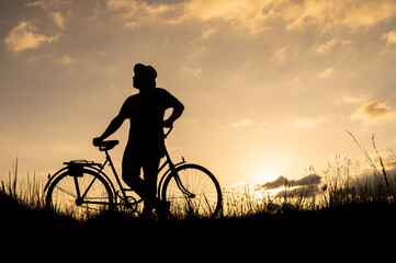 Silhouette of a man on a bike or bicycle and looking back. Setting sun background.
