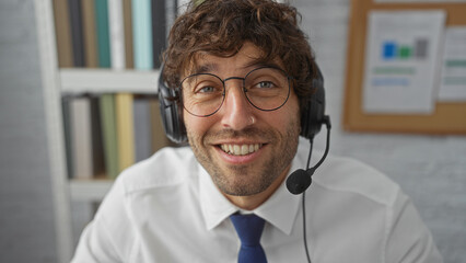 Young man with headset smiling in an office setting, embodying professionalism and approachability in a modern work environment.