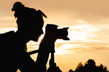 Close-up silhouette portrait of a young female photographer looking through the viewfinder of a...