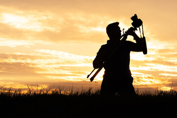 Silhouette of Man Holding Tripod and Camera at Sunset in Nature Field