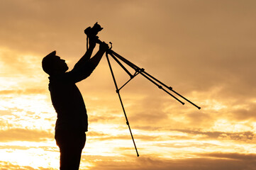 Man Holding Camera and Tripod Silhouette Against Vibrant Sunset Sky.