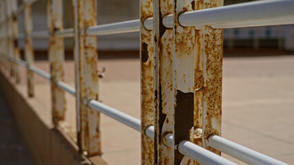 Rusty metal fence outdoors on a sunny day, displaying weathered texture and decay in a bright urban setting.