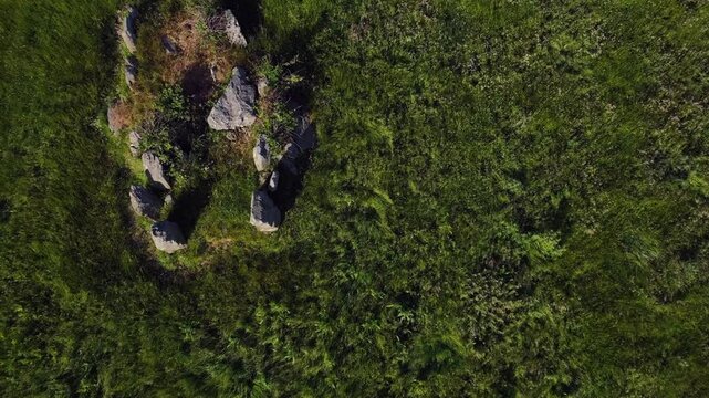Lisnadarragh Wedge Tomb, County Monaghan, Ireland, June 2023. Drone ascend tilting down above megalithic roofless burial site from neolithic era in grassy field with long shadows from afternoon sun
