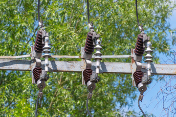 Electric power lines with insulators among green trees under clear blue sky