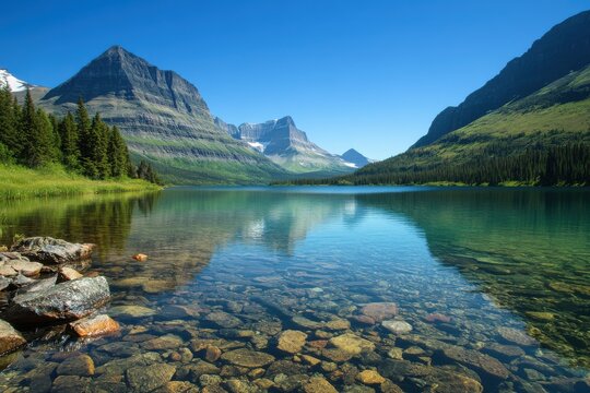 A scenic view of a clear lake reflecting mountains and sky with rocks visible in the foreground water