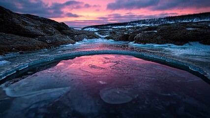 Scenic landscape featuring a frozen pool reflecting a vibrant pink and purple sunset, surrounded by ice-covered rocks and distant trees, capturing the serene beauty of a cold, arctic twilight - Powered by Adobe