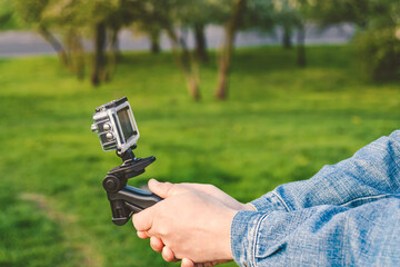 An action camera with a tripod in the hands of a man against the backdrop of a lawn of grass and...