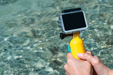A camera with a waterproof case in the hands of a girl. Against the background of the water in the...