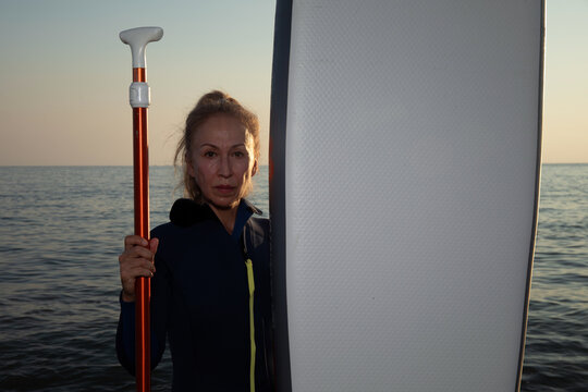 Old oman in wetsuit with surfing board or sup, beach. Senior lady having active lifestyle at sea