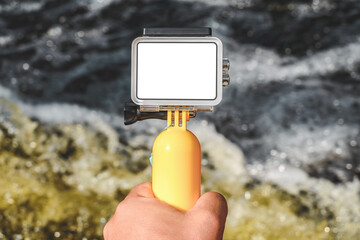 Action camera mockup with a yellow float in a male hand. Background of water and waves.