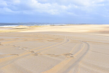 A big bright yellow sand dune on the background of bright cloudy sky. Something like a hieroglyph on the surface. Stockton Sand Dunes near the coast, Worimi Regional Park, Anna Bay, Australia. 