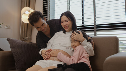 lovely family spend time together in their house, a pregnant mother sits on the couch with her...