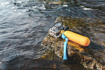 A waterproof photo-video action camera lies on a rock in the water. Time for a healthy lifestyle in...