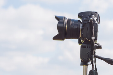 Professional photo-video camera close-up on the background of the sky with clouds.