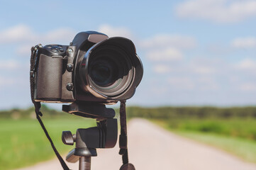 Close-up of a camera on a tripod. Background of the road on the field.