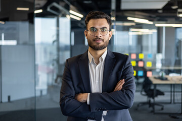 Portrait of serious confident businessman at workplace inside office. Man with crossed arms looking...