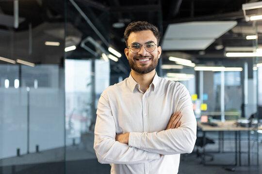 Portrait of successful young businessman man smiling and looking at camera with crossed arms. Office worker satisfied with results of achievement at workplace.