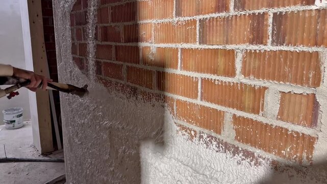 Construction Worker Spraying Plaster on Interior Brick Wall