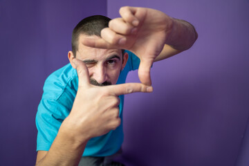 Young handsome man doing frame using hands palms and fingers, over purple background. High quality photo