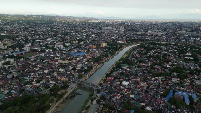 Drone panoramic ascend of Marikina river slicing through residential areas with traffic during daytime, dense urban sprawl