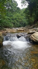 Flowing river cascading over rocks in lush green tropical forest at sunny day eye level shot in Malaysia