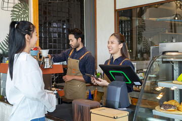 Asian cafe cashier worker female showing menu or cashless billing payment to customer, barista small business owner using technology tablet receives coffee order at workplace in restaurant coffee shop