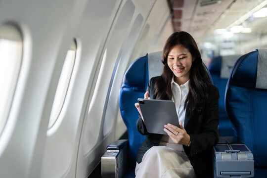 Business travel with young woman smiling while using tablet on airplane