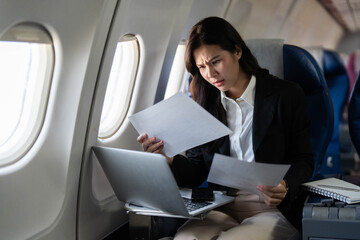 Business travel: Concerned professional woman evaluating documents on airplane