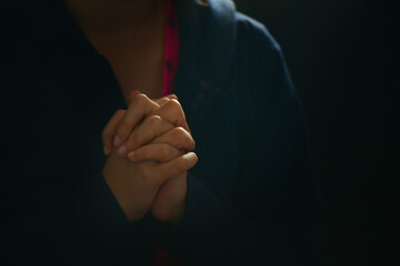 Woman with hands clasped standing against black background