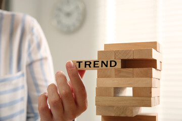 Woman removing wooden block with word Trend from tower indoors, closeup